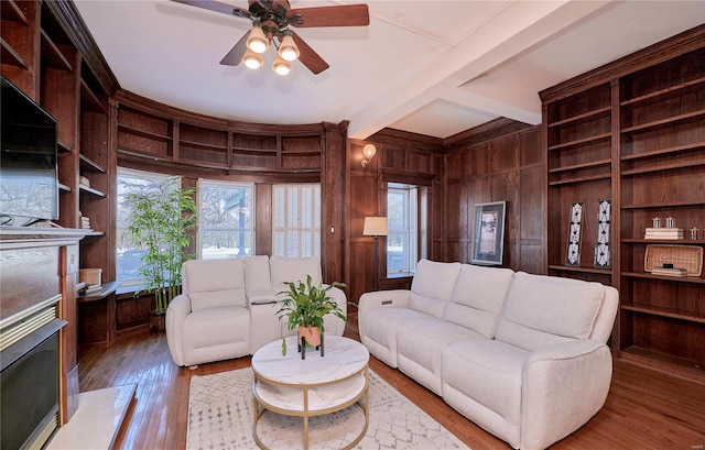 living room featuring a fireplace with raised hearth, beamed ceiling, wood walls, hardwood / wood-style floors, and a ceiling fan