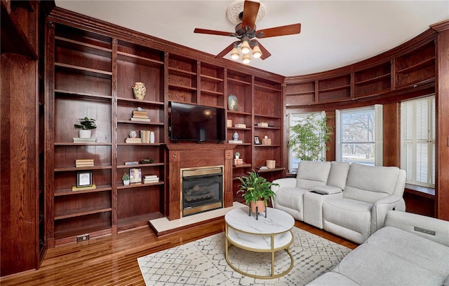 living area with ceiling fan, wood finished floors, and a glass covered fireplace