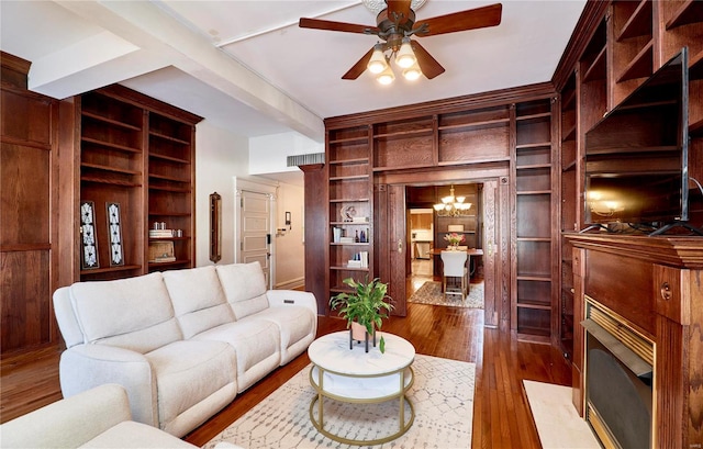 living area with beam ceiling, built in features, ceiling fan with notable chandelier, and wood-type flooring