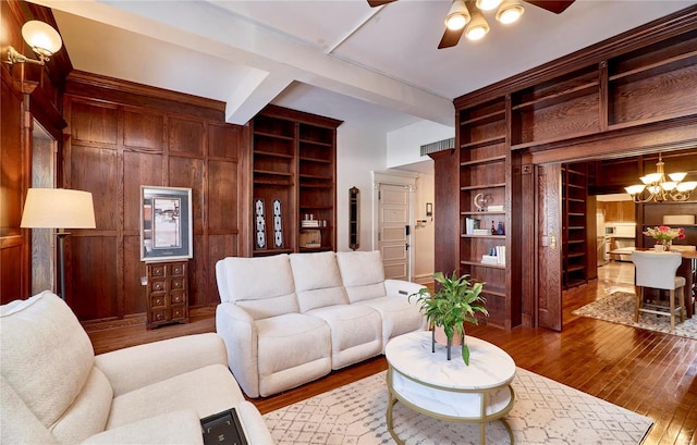 living area featuring hardwood / wood-style floors, wooden walls, built in features, and ceiling fan with notable chandelier