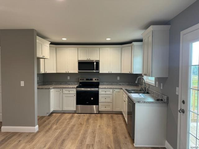 kitchen with sink, white cabinetry, light stone counters, light wood-type flooring, and appliances with stainless steel finishes