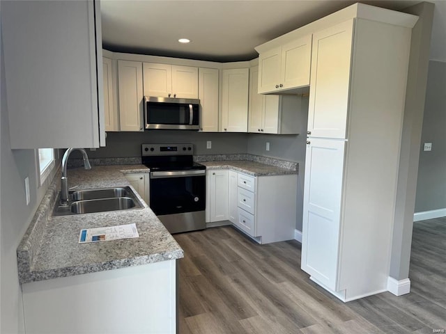 kitchen with stainless steel appliances, sink, white cabinetry, hardwood / wood-style floors, and light stone countertops