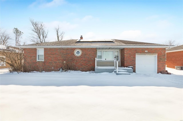 snow covered rear of property featuring solar panels and a garage