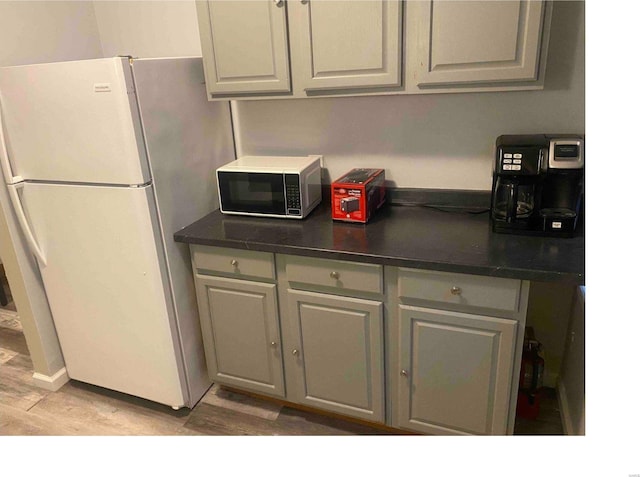 kitchen with light wood-type flooring, white fridge, and gray cabinetry