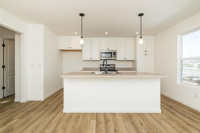 kitchen with pendant lighting, stainless steel appliances, an island with sink, and white cabinets