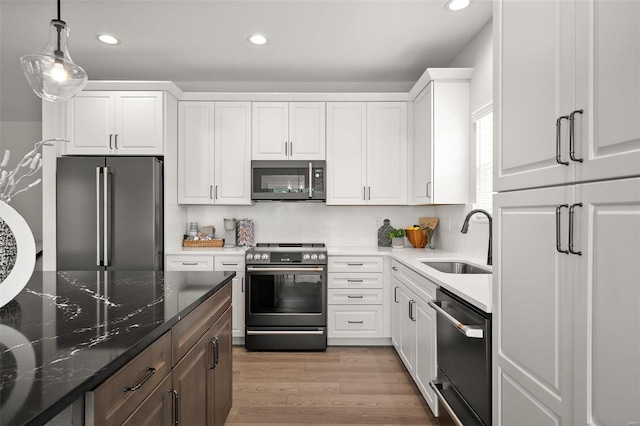 kitchen with stainless steel appliances, sink, light hardwood / wood-style flooring, dark stone countertops, and white cabinetry