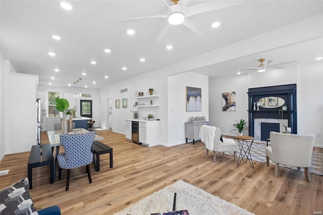 living room with ceiling fan, beverage cooler, recessed lighting, light wood-style flooring, and a fireplace