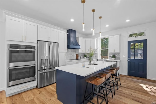 kitchen with light countertops, a kitchen breakfast bar, stainless steel appliances, custom exhaust hood, and white cabinetry