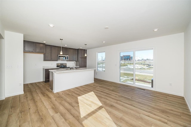 kitchen featuring light hardwood / wood-style floors, appliances with stainless steel finishes, hanging light fixtures, a kitchen island with sink, and sink