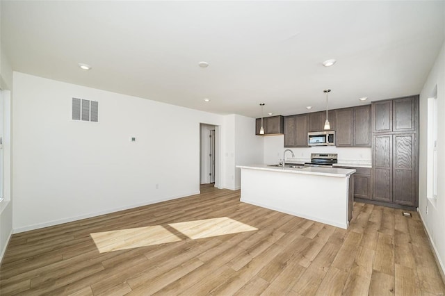 kitchen featuring sink, light wood-type flooring, pendant lighting, an island with sink, and stainless steel appliances