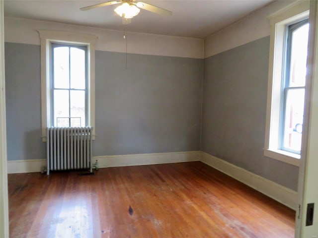 empty room with ceiling fan, wood-type flooring, radiator heating unit, and a wealth of natural light