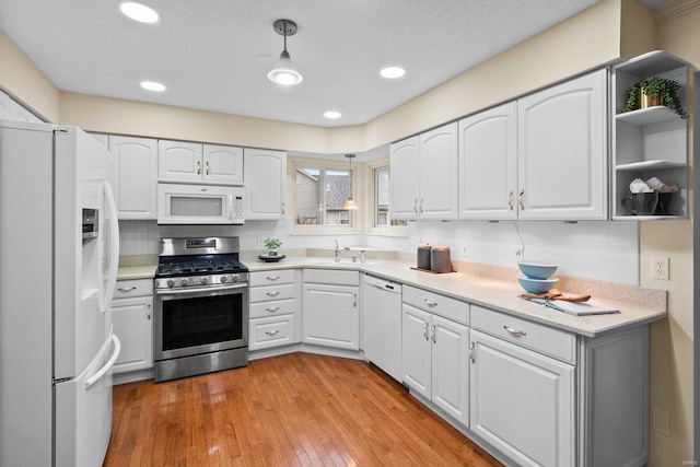 kitchen featuring white cabinetry, sink, hanging light fixtures, white appliances, and light hardwood / wood-style flooring