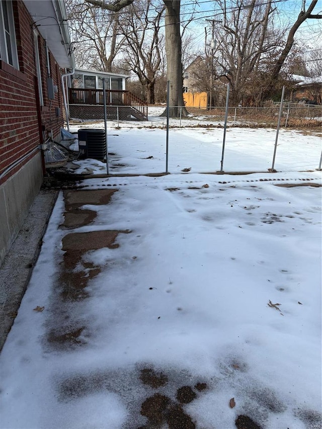 yard covered in snow with central air condition unit and a sunroom