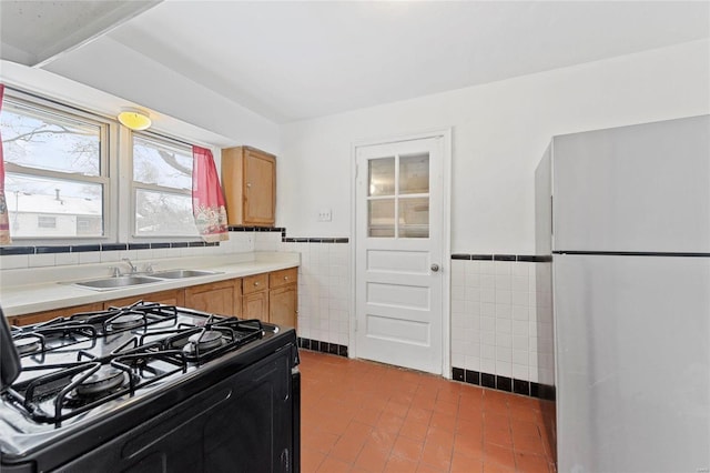 kitchen featuring tile walls, sink, black range with gas stovetop, and stainless steel fridge