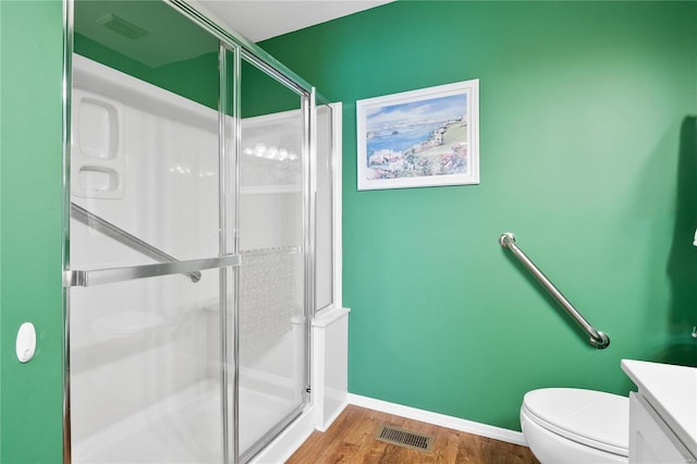 bathroom featuring hardwood / wood-style flooring, toilet, a shower with shower door, and vanity