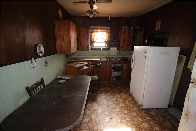 kitchen featuring white refrigerator, ceiling fan, wood walls, and sink