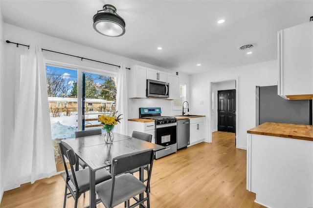 kitchen with stainless steel appliances, sink, light hardwood / wood-style flooring, butcher block countertops, and white cabinetry