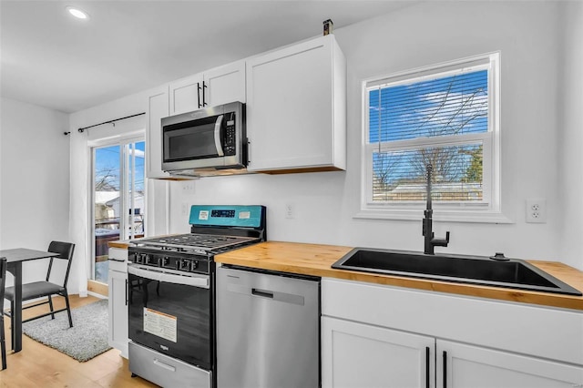 kitchen with light wood-type flooring, stainless steel appliances, sink, white cabinets, and plenty of natural light