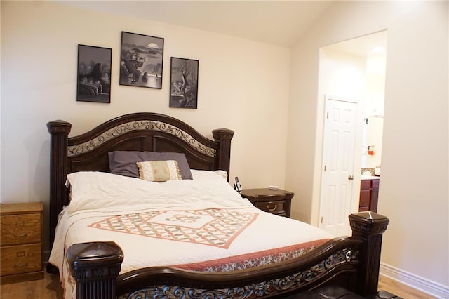 bedroom with ensuite bath, lofted ceiling, and hardwood / wood-style flooring