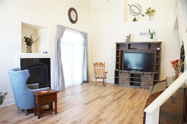 living area featuring hardwood / wood-style flooring, a towering ceiling, and a tiled fireplace