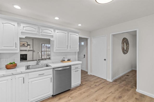 kitchen featuring sink, white cabinets, stainless steel dishwasher, a brick fireplace, and light wood-type flooring