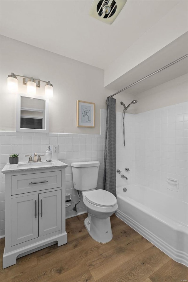 full bathroom with tile walls, hardwood / wood-style floors, vanity, shower / bath combination with curtain, and toilet