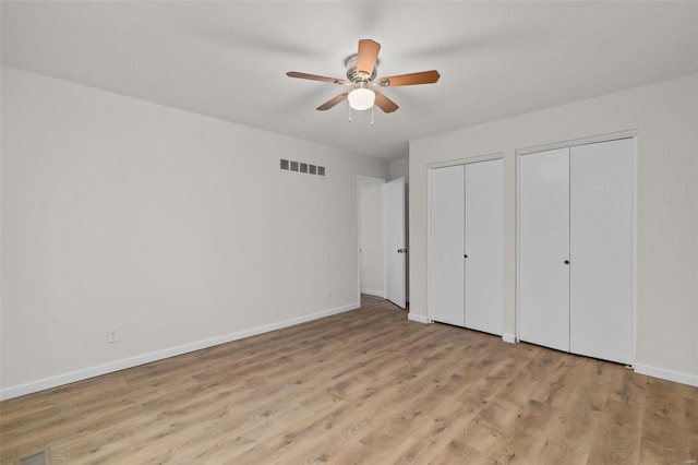 unfurnished bedroom with two closets, light hardwood / wood-style floors, and ceiling fan