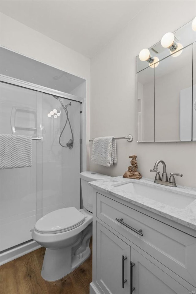 bathroom with vanity, hardwood / wood-style flooring, a shower with door, and toilet