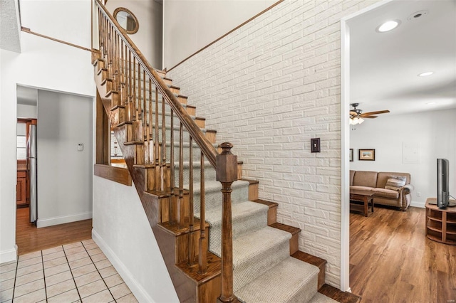 stairway featuring a towering ceiling, brick wall, baseboards, and wood finished floors