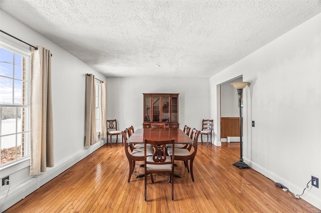 dining area with light wood-style floors, a textured ceiling, and baseboards