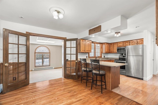 kitchen featuring appliances with stainless steel finishes, brown cabinetry, a baseboard heating unit, light wood-type flooring, and a peninsula