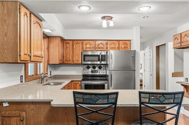 kitchen with stainless steel appliances, a peninsula, a sink, and brown cabinets