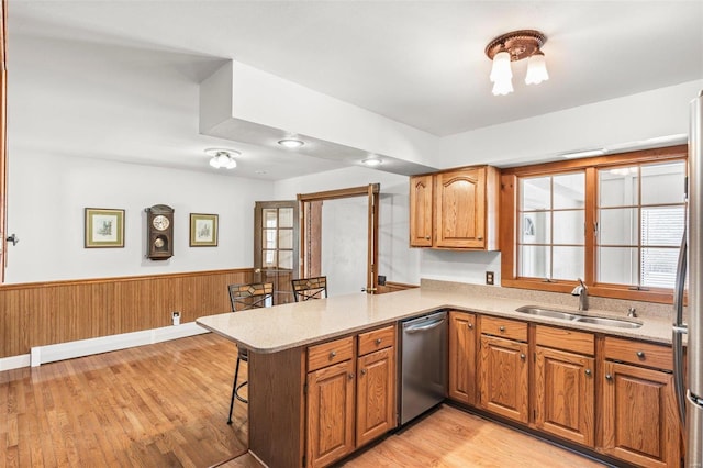 kitchen featuring dishwasher, a wainscoted wall, a breakfast bar area, a peninsula, and a sink