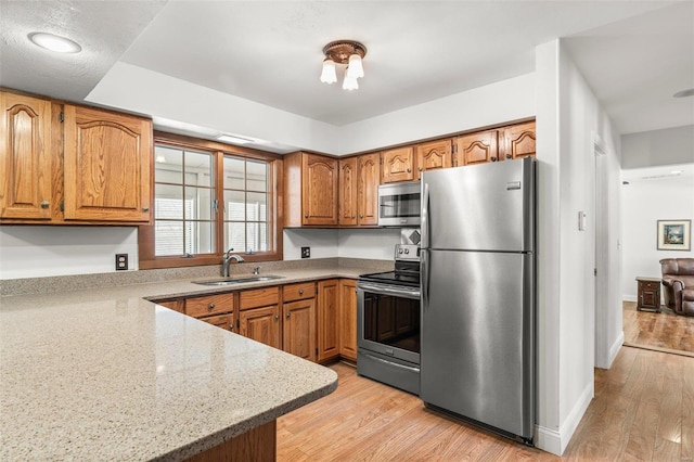 kitchen with appliances with stainless steel finishes, brown cabinetry, a sink, and light wood-style floors