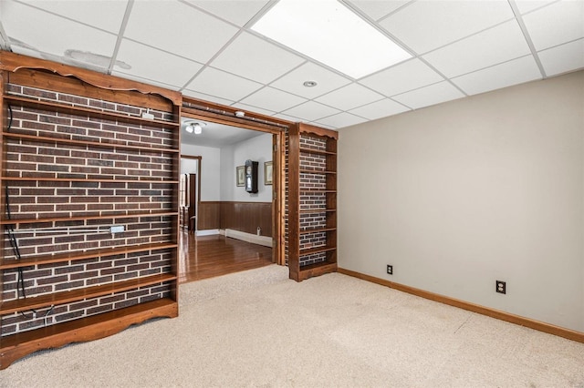 carpeted empty room with wood walls, a drop ceiling, and wainscoting