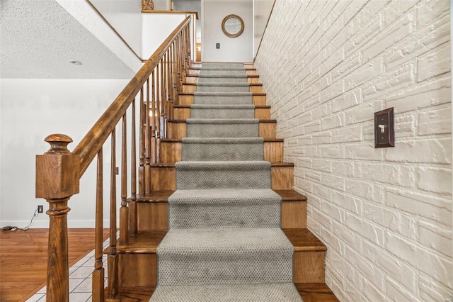 staircase featuring baseboards, a textured ceiling, brick wall, and wood finished floors