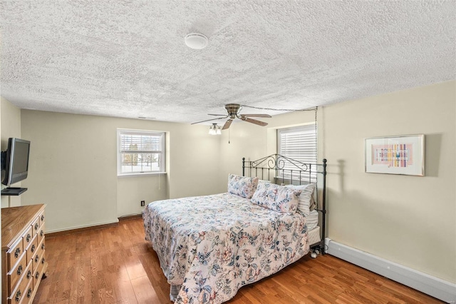 bedroom featuring ceiling fan, a baseboard radiator, wood finished floors, and baseboards