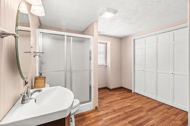 bathroom with a textured ceiling, a stall shower, wood finished floors, and baseboards