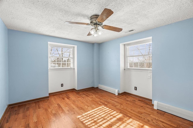 unfurnished room featuring a baseboard heating unit, a wealth of natural light, visible vents, and wood finished floors