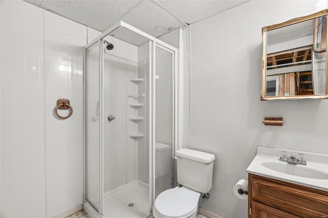 bathroom with a stall shower, vanity, toilet, and tile walls