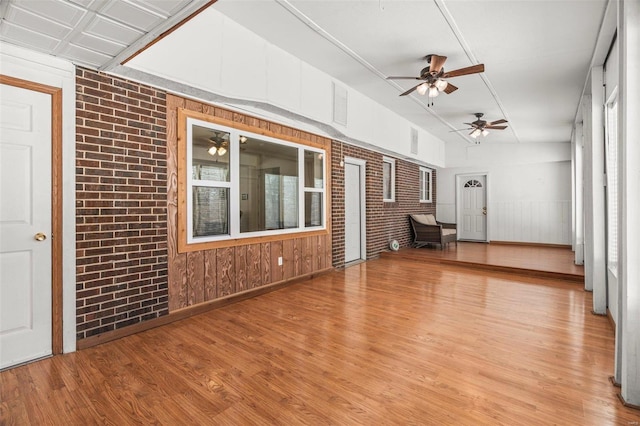 unfurnished living room featuring ceiling fan, brick wall, and light wood-type flooring