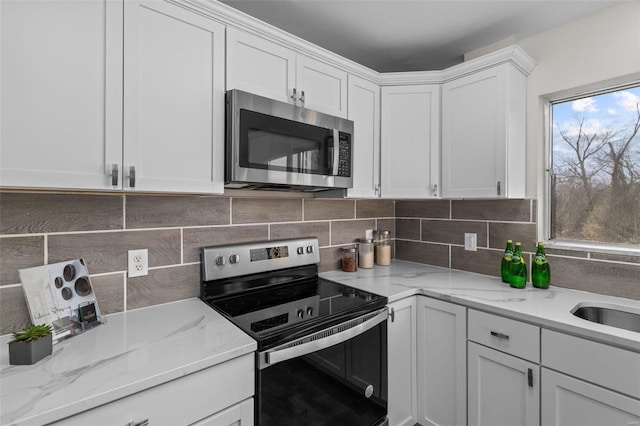 kitchen with appliances with stainless steel finishes, backsplash, light stone countertops, white cabinetry, and a sink