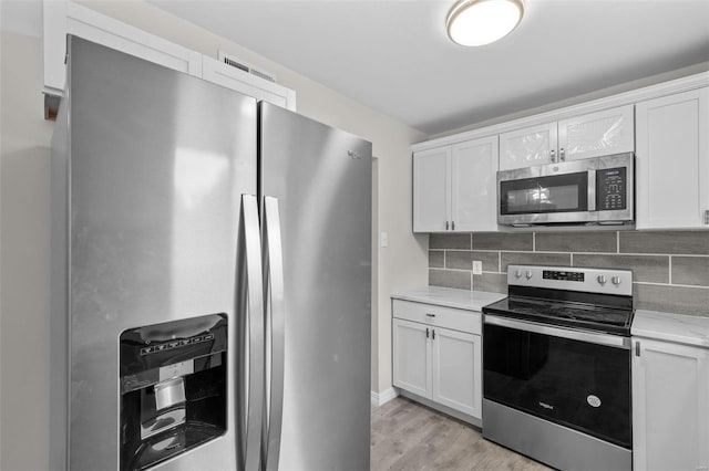 kitchen featuring appliances with stainless steel finishes, light wood-style flooring, backsplash, and white cabinetry