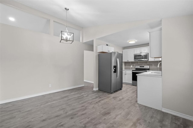 kitchen featuring light countertops, backsplash, appliances with stainless steel finishes, light wood-style floors, and white cabinets