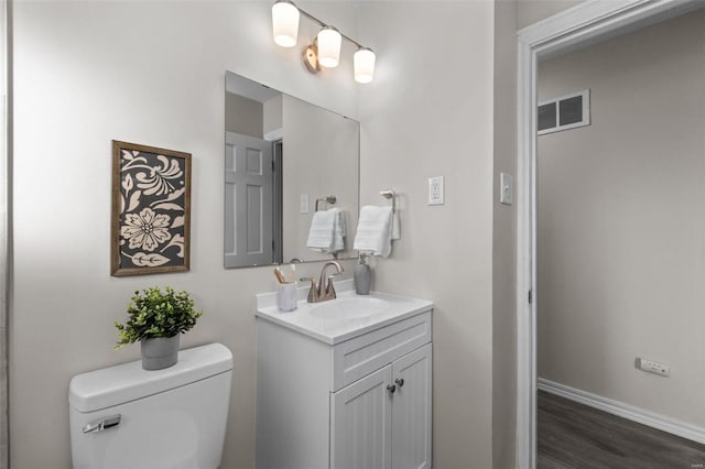 half bathroom with toilet, wood finished floors, vanity, visible vents, and baseboards