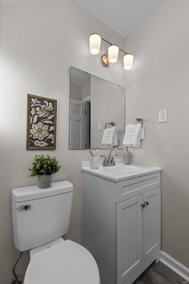 half bath with baseboards, vanity, toilet, and wood finished floors