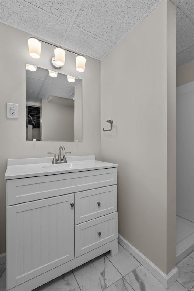 bathroom with marble finish floor, baseboards, a drop ceiling, and vanity