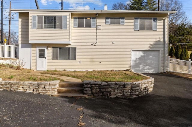 rear view of house featuring a garage, driveway, and fence