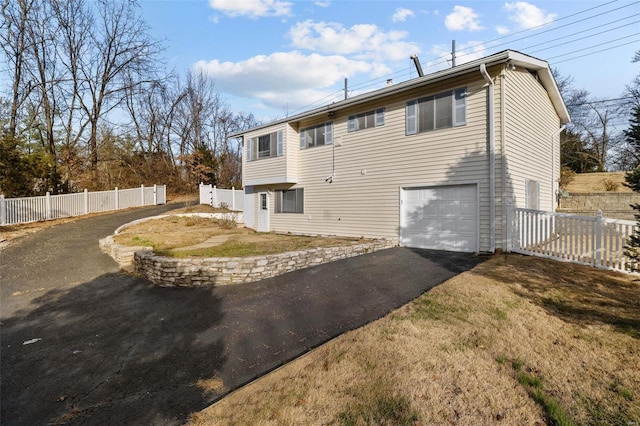 rear view of property featuring driveway, an attached garage, and fence