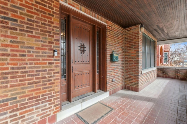 doorway to property with covered porch and brick siding